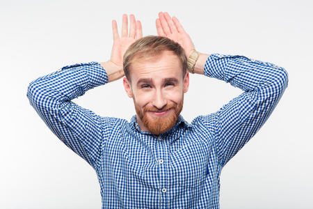 Portrait of a funny casual man showing rabbit geture over his head isolated on a white backgroundの写真素材