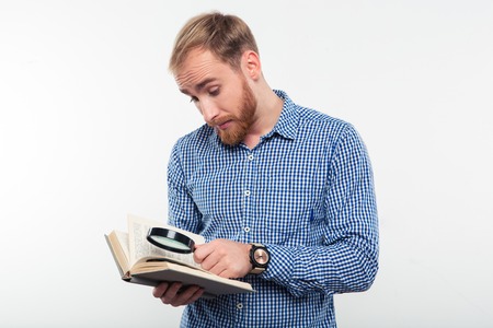 Portrait of young man reading book with magnifying glass isolated on a white backgroundの写真素材