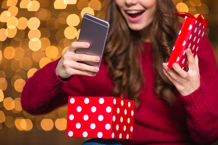 Happy amazed young woman in santa claus hat opened present and got a smartphone over sparkling...