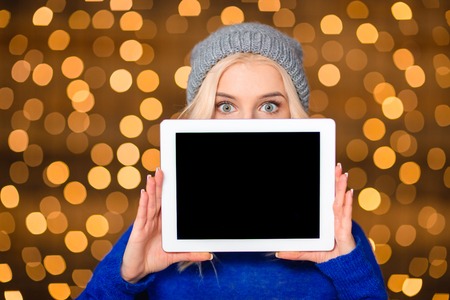 Portrait of a young woman showing blank tablet computer screen over holdays lights backgroundの写真素材