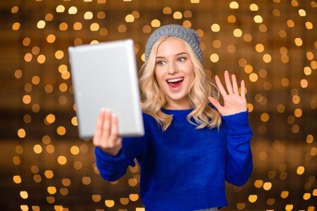 Portrait of a cheerful woman doing video call on tablet computer over holiday lights on background