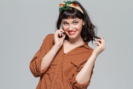 Beautiful cheerful young woman talking on cellphone isolated over grey backgroundの写真素材