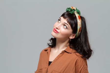 Cute lovely young female dreaming and looking up isolated over grey backgroundの写真素材