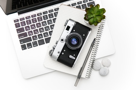 Top view of laptop and notepad with pan lying under vintage old camera and green flover over white backgroundの写真素材