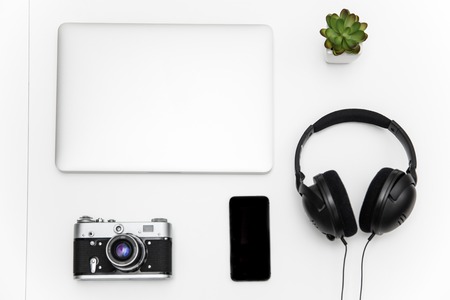 Top view of laptop, blank screen smartphone, vintage camera, headset  and green flower on white backgroundの写真素材