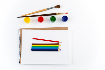 Top view of sketchbook, paintbrushes, colorful pensils and gouache paints isolated over white backgroundの写真素材