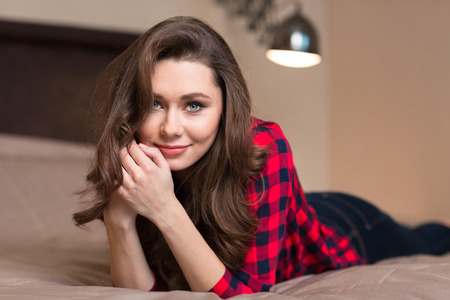 Portrait of a young attractive woman in casual cloth lying on the bed and looking at cameraの写真素材
