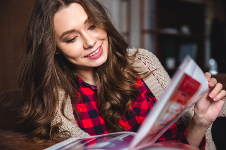 Portrait of a smiling woman reading magazine at homeの写真素材