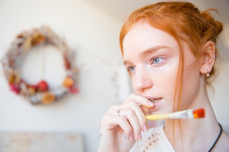 Portrait of pensive beautiful young female holding paintbrush and thinkingの写真素材