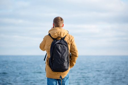 Back view portrait of a man with backpack talking on the phone with sea on backgroundの写真素材