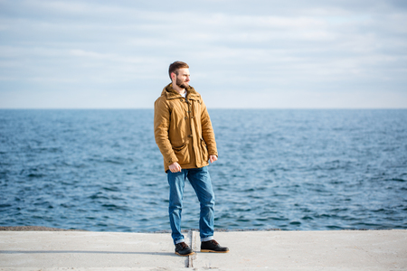 Full length portrait of a thoughtful man standing on pier near the seaの写真素材