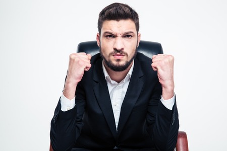 Angry annoyed bearded businessman in black jacket and white shirt sitting and showing fists over white backgroundの写真素材