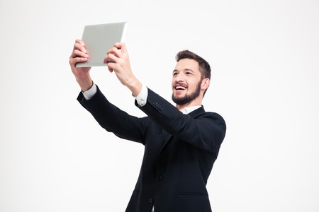 Portrait of a cheerful businessman making selfie photo on tablet computer isolated on a white backgroundの写真素材
