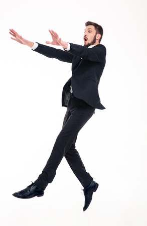 Stunned afraid young bearded businessman in black suit flying with strong wind blowing on him over white backgroundの写真素材