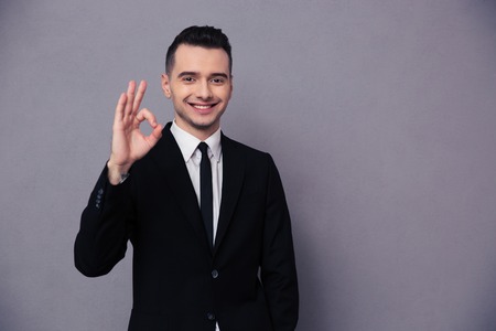 Portrait of a smiling businessman showing ok sign over gray backgroundの写真素材