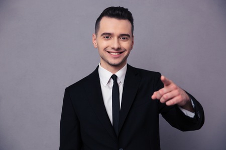 Portrait of a smiling businessman pointing finger at camera over gray backgroundの写真素材