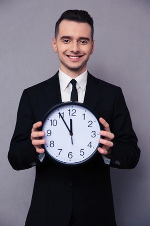 Portrait of a smiling businessman holding wall clock over gray backgroundの写真素材
