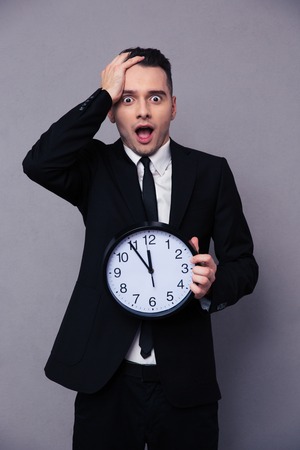 Amazed businessman holding wall clock over gray backgroundの写真素材