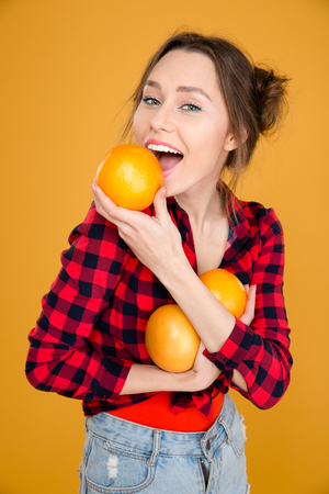Beautiful smiling young woman in plaid shirt holding grapefruits over yellow backgroundの写真素材