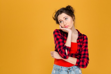Portrait of sad depressed beautiful young woman in plaid shirt over yellow backgroundの写真素材