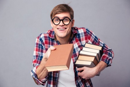 Playful happy young man in checkered shirt and funny round glasses giving youn a book over grey backgroundの写真素材