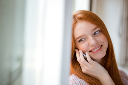 Portrait of a smiling redhead woman talking on the phone and looking at cameraの写真素材