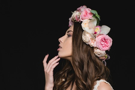 Profile of sensual young woman with long curly hair in flower wreath over black background