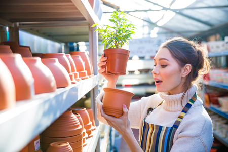 Pensive charming young woman gardener choosing new pot for her plant in storeの写真素材