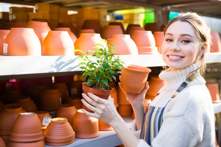 Happy lovely young woman gardener buying new pot for her plant in the shopの写真素材
