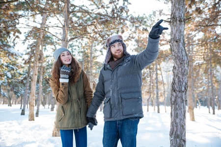 Handsome man walking with his girlfriend in winter park and pointing up