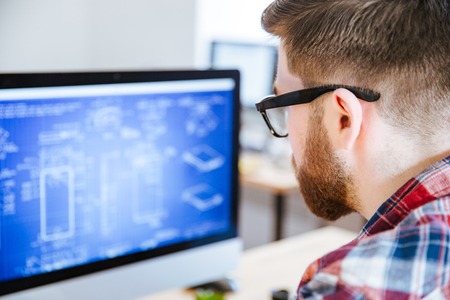 Closeup of young man in glasses with beard making blueprints on computerの写真素材