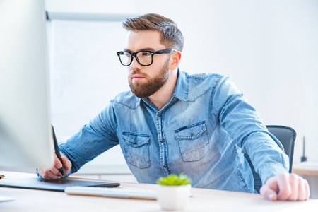 Serious concentrated young man designer drawing with graphic pen tablet using stylus in office