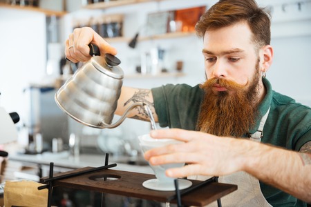 Barista pouring water on coffee ground with filter in coffee shopの写真素材