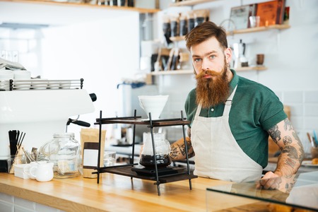 Barista preparing coffee in coffee shop and looking at cameraの写真素材