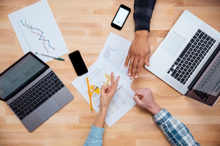 Multiethnic group of young people woking for monthly budget with laptops and gesturing rock paper scissors gameの写真素材