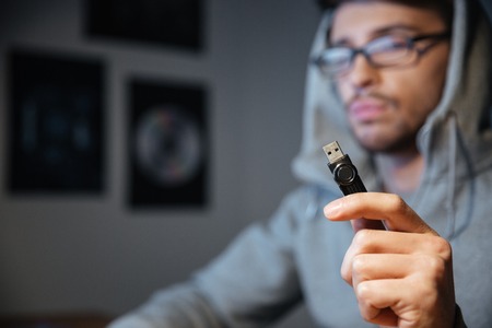 Handsome young man in glasses sitting in the room and holding usb cable