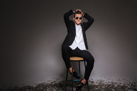 Handsome man in trendy cloth sititng on the chair over black backgroundの写真素材