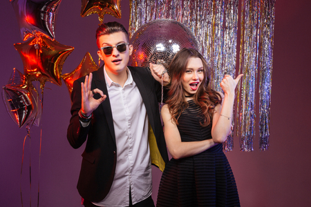 Beautiful young couple having party and showing thumbs up and ok gesture over purple backgroundの写真素材
