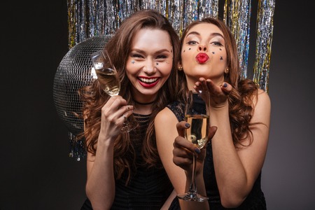 Cheerful beautiful young women having party and sending kiss over black backgroundの写真素材