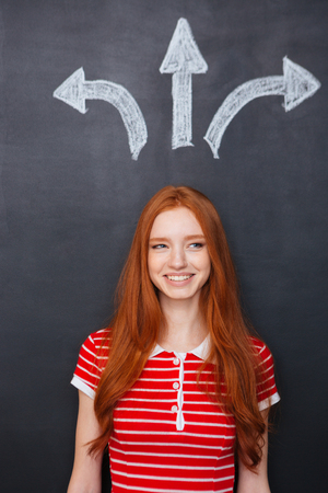Beautiful cheerful redhead woman making decision standing over chalkboard backgroundの写真素材