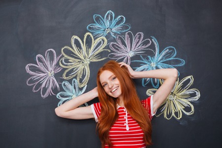 Happy cute lovely young woman standing over chalkboard with drawn colorful flowersの写真素材