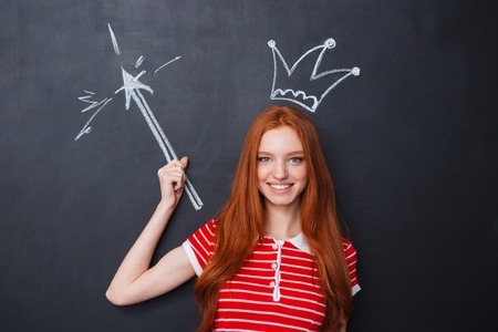 Happy beautiful young woman with crown and magic drawn on blackboard backgroundの写真素材