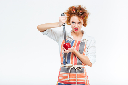 Housewife cutting apple with big knife isolated on a white backgroundの写真素材