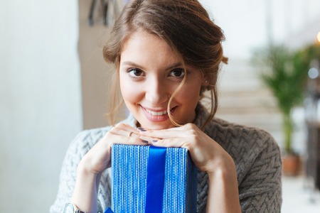 Closeup portrait of a smiling woman with gift box looking at cameraの写真素材