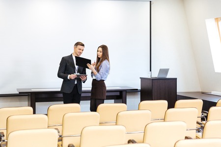 Businessman and businesswoman standing and working in empty meeting hall