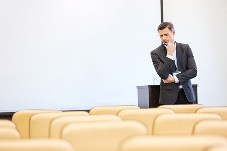 Thoughtful serious businessman standing and thinking in empty conference hallの写真素材