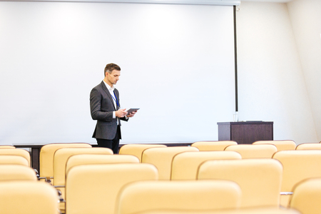Handsome concentrated speaker repeating his speech and using tablet in empty boardroomの写真素材