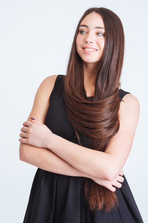 Closeup of smiling gorgeous young woman with long dark hair standing with hands folded over white backgroundの写真素材