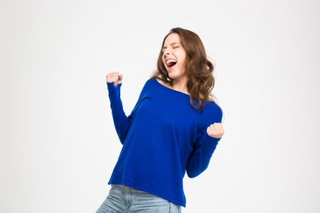 Excited delighted young woman shouting and celebrating success over white backgroundの写真素材