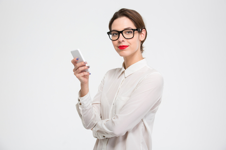Happy confident young business woman in glasses using smartphone over white backgroundの写真素材